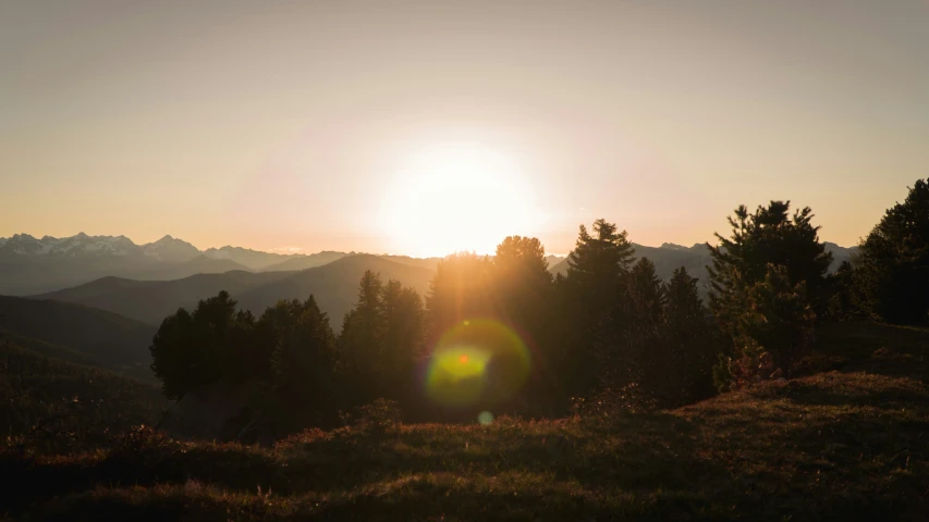 the sun is setting over mountains and trees