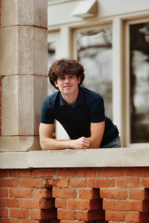 a young man leaning on a brick wall with his hand on his hips