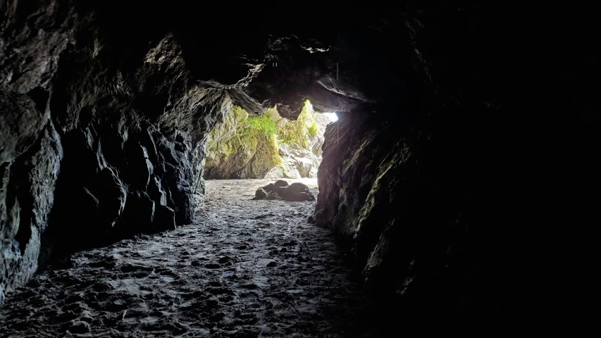 a dark cave tunnel with a beach at the end