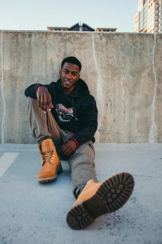 a black man wearing brown boots sitting on a cement wall