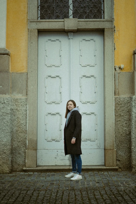 a woman standing in front of a door wearing a black coat