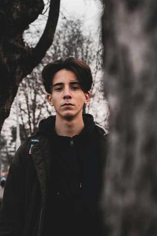 a young man standing next to a tree