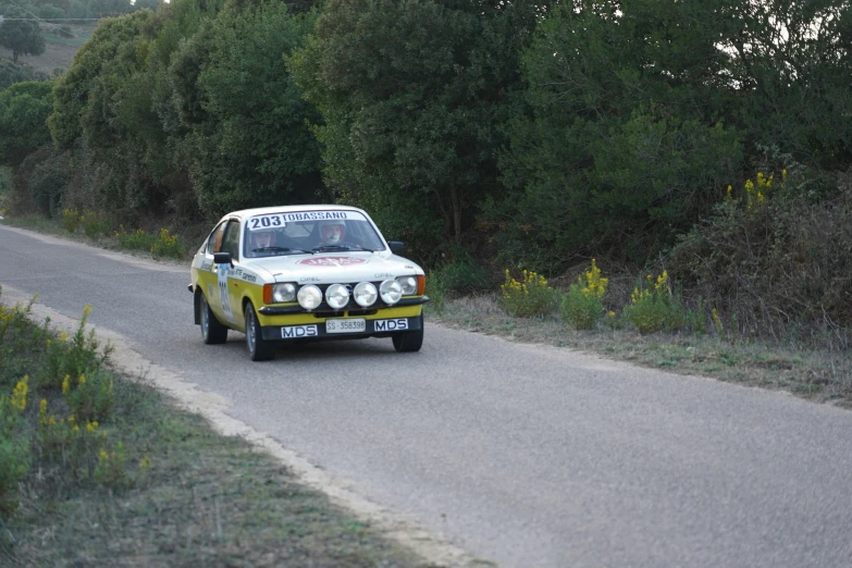 a classic car driving down a road next to trees