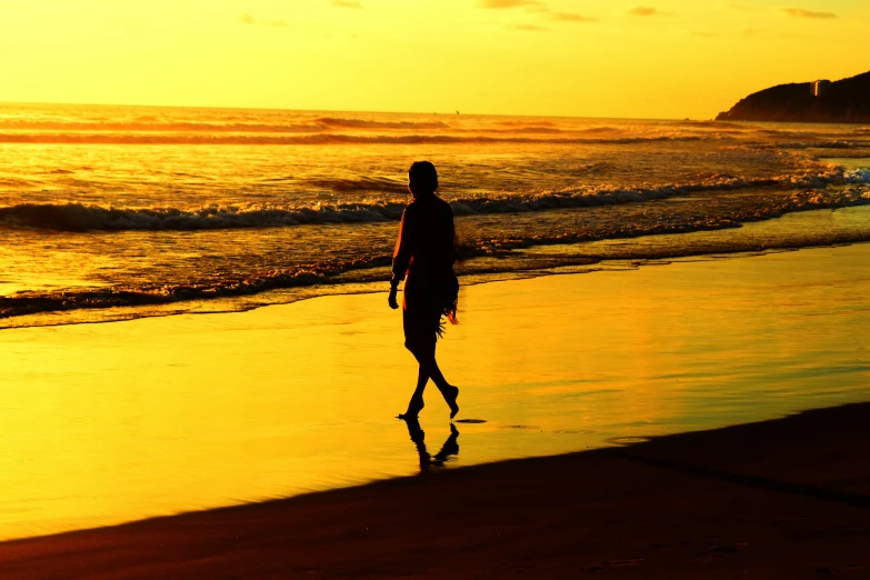 a man is walking on the beach at sunset