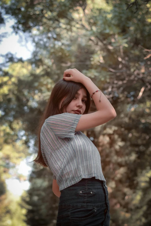 a girl wearing an over shirt standing under trees