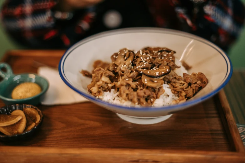 a wooden board topped with a bowl filled with rice and meat