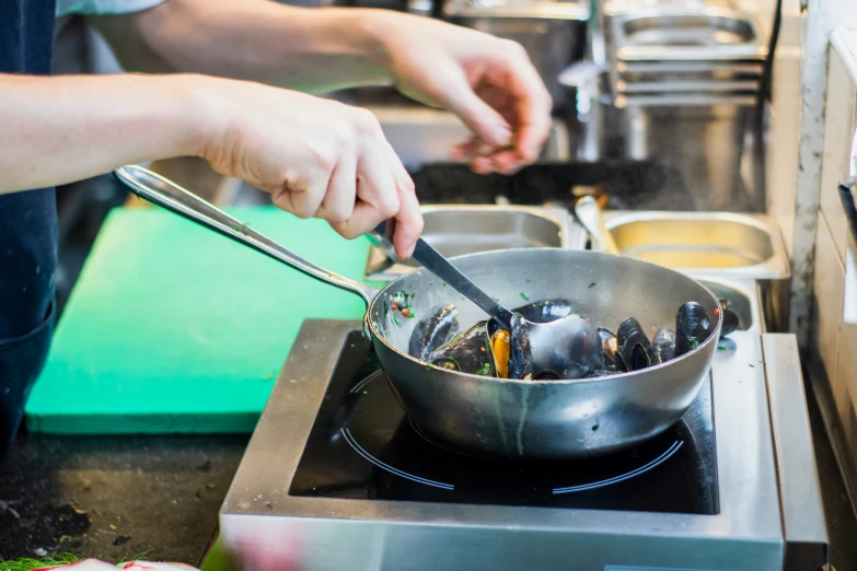 person stirring a pan with clams to prepare meal