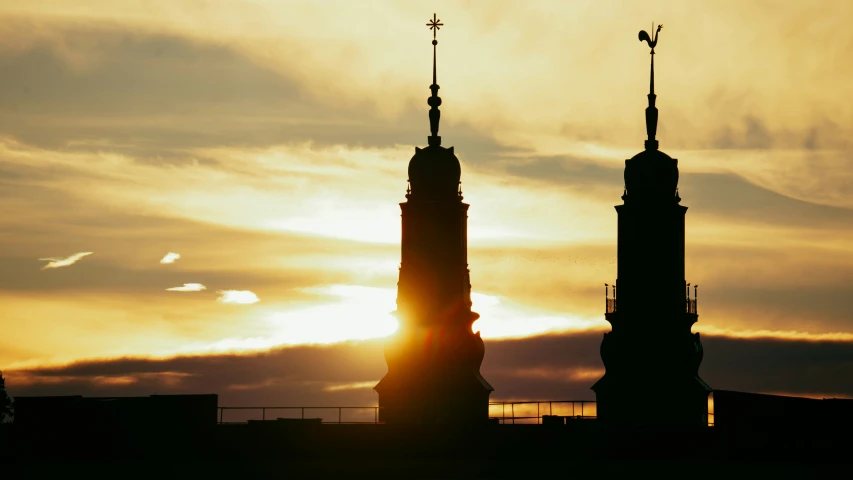 the two towers are silhouetted against the sun setting