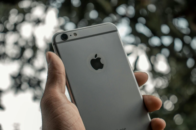 a person's hand holding an iphone in front of trees