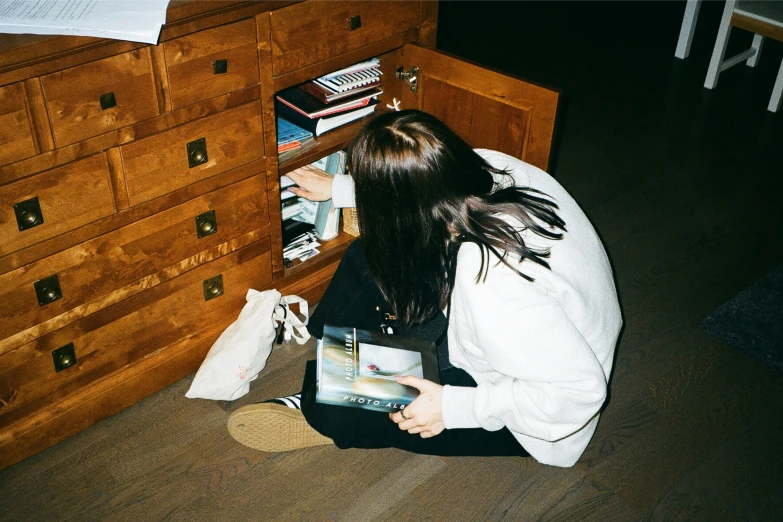 a woman sitting down on the floor and leaning up against an empty drawer