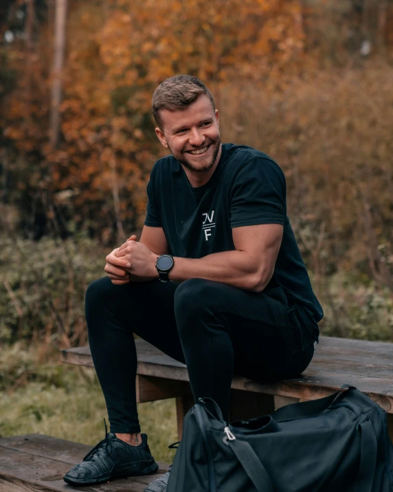 a smiling man sits on a bench with his luggage
