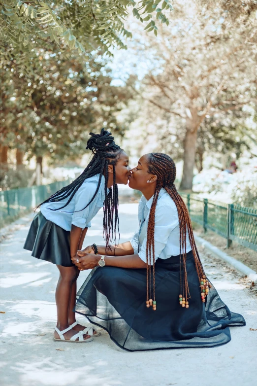 two girls are touching noses outside near trees