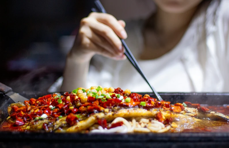 someone holds chopsticks over a large pan with chinese food