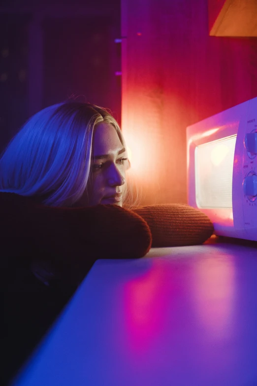 a blonde woman sitting at a table with a microwave