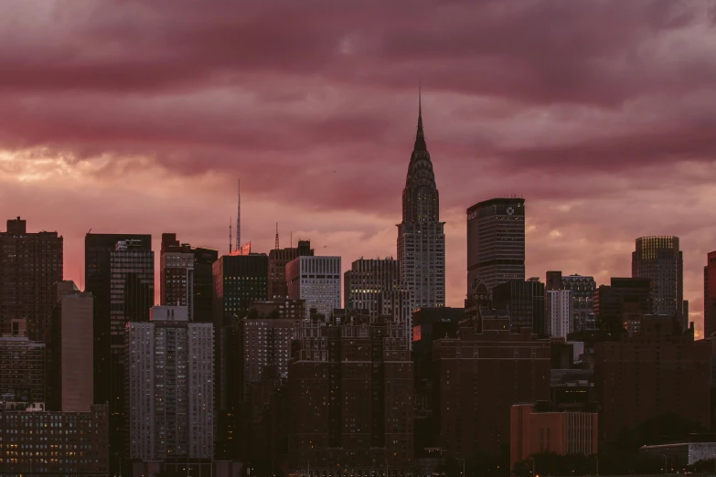 the skyline of new york city at sunset with clouds and dark, red tones