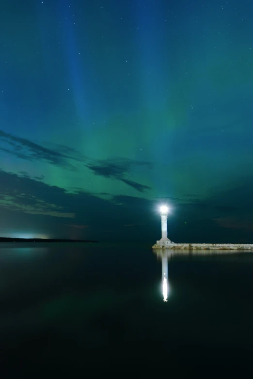 the lighthouse and aurora lights are reflecting on the water