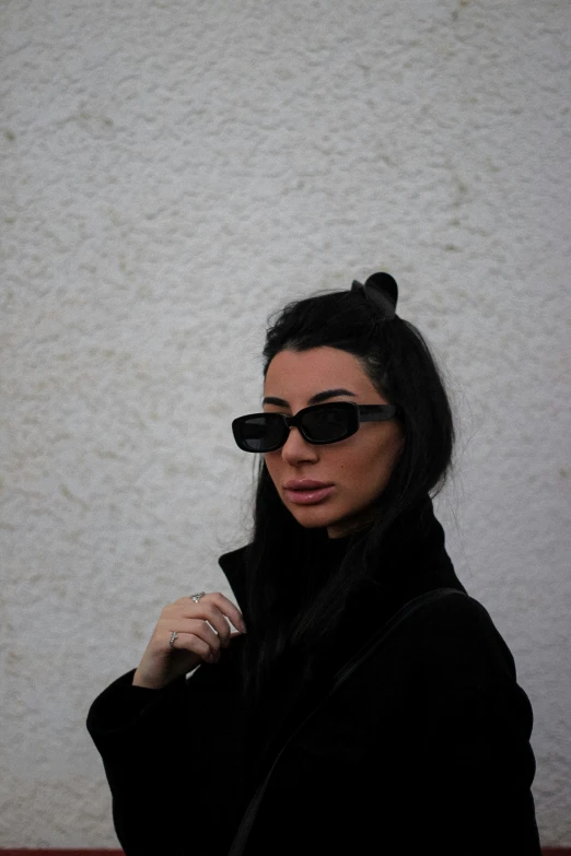 a woman is in front of a wall with sunglasses on