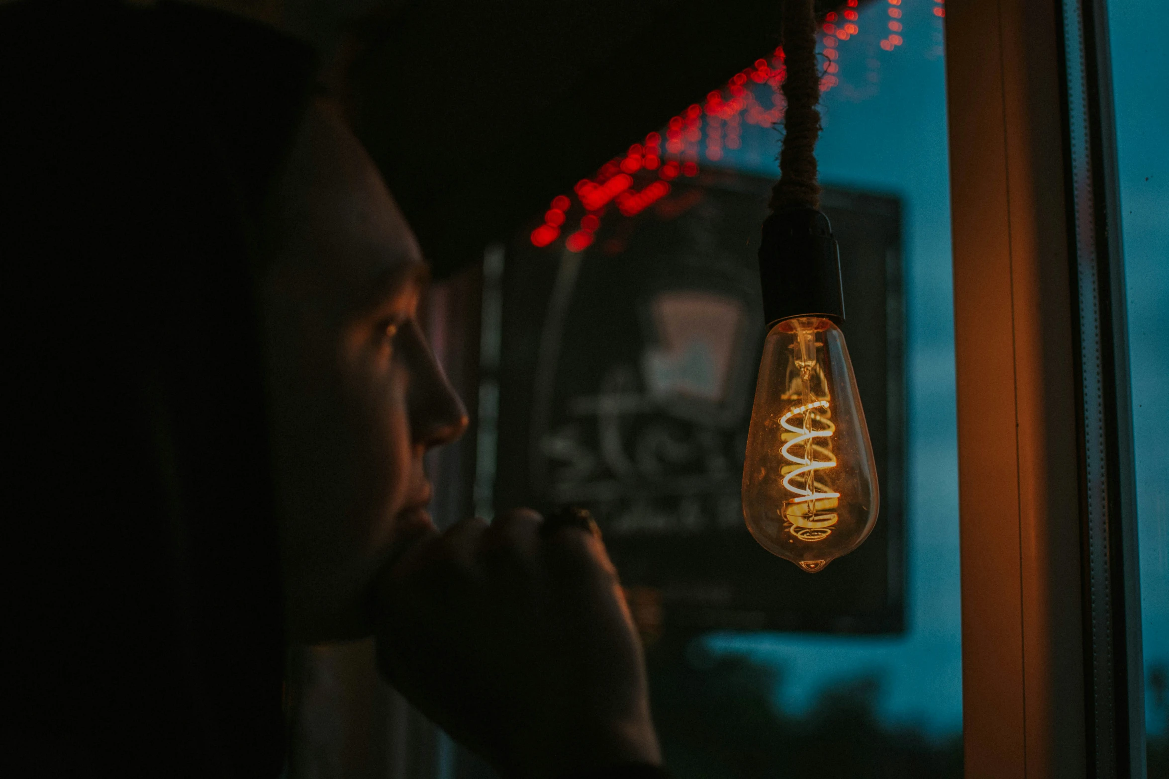 a person looking out a window at a light bulb hanging from a ceiling