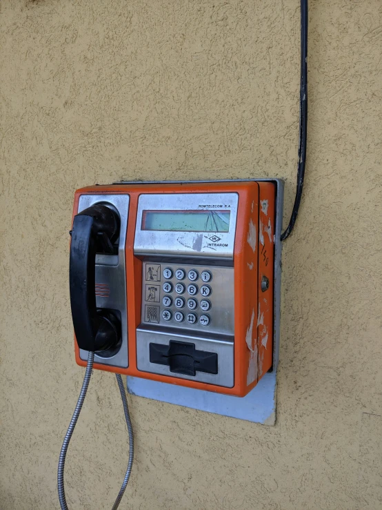 a pay phone on the wall with cord to it