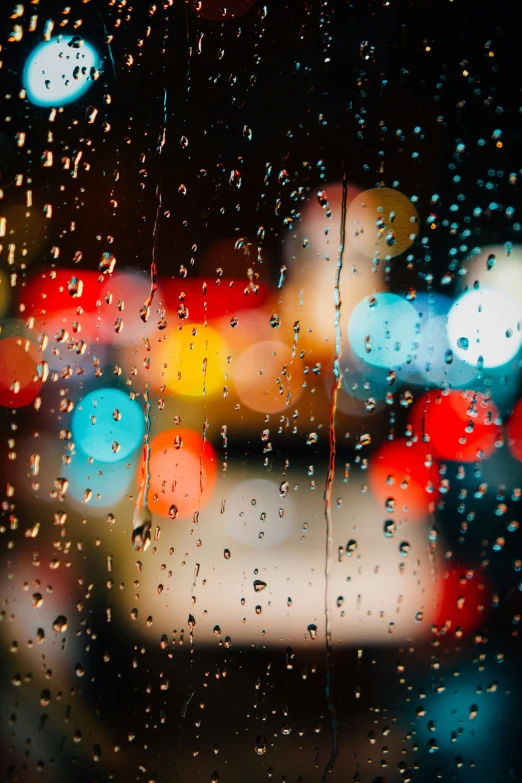 a rain - streaked window with some blurred cars outside