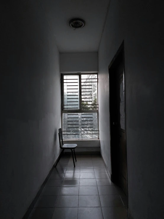 a white hallway with a window, tiled floor and black door