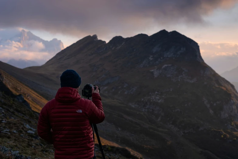 a man in red jacket with a camera taking pictures on the side of a mountain