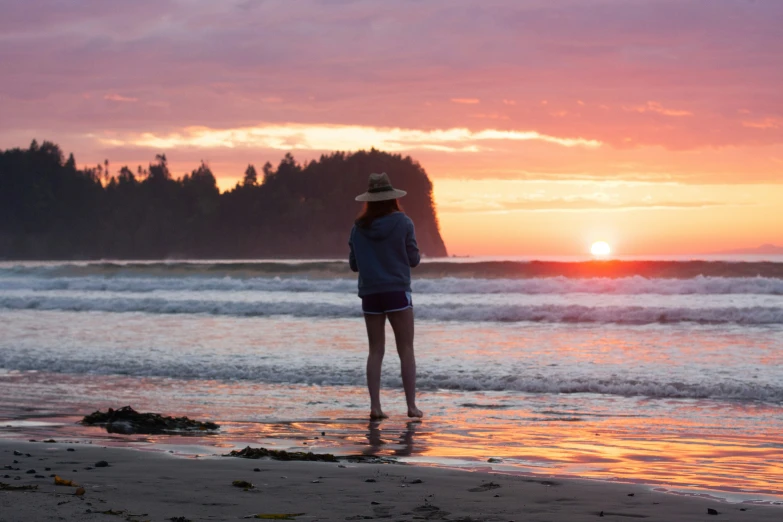 a woman stands in the ocean looking into the sunset