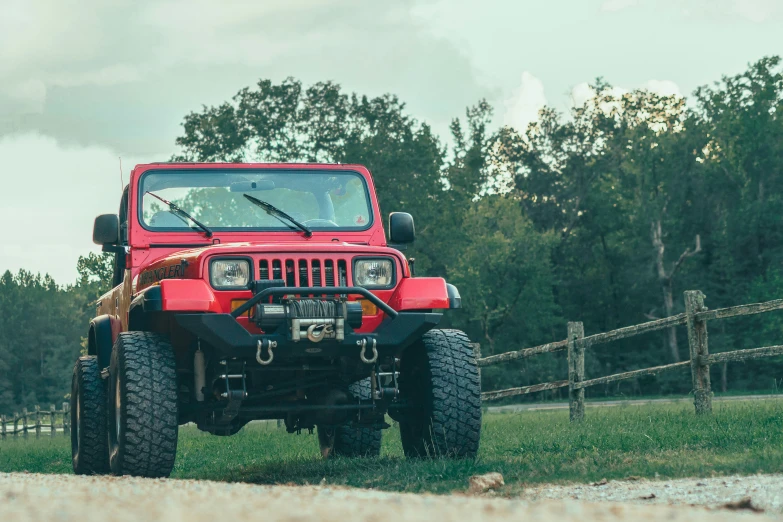 a red jeep is driving down a dirt road