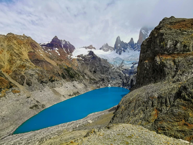 a lake surrounded by mountains under a cloudy sky