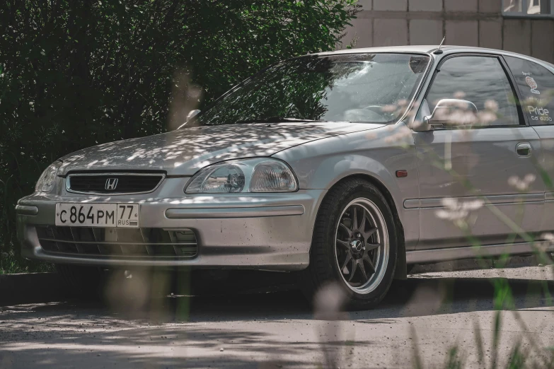 the silver car is parked near a tree and bushes