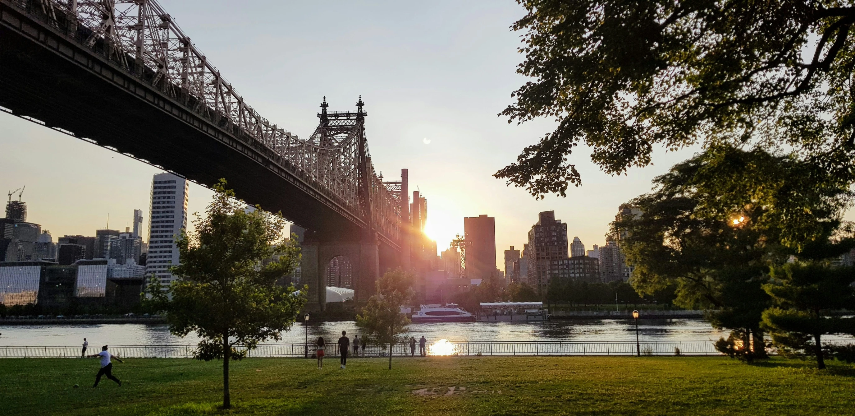 the sun is setting over a river with tall buildings