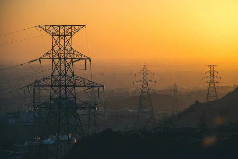 many electricity towers over a city with sun rising behind them