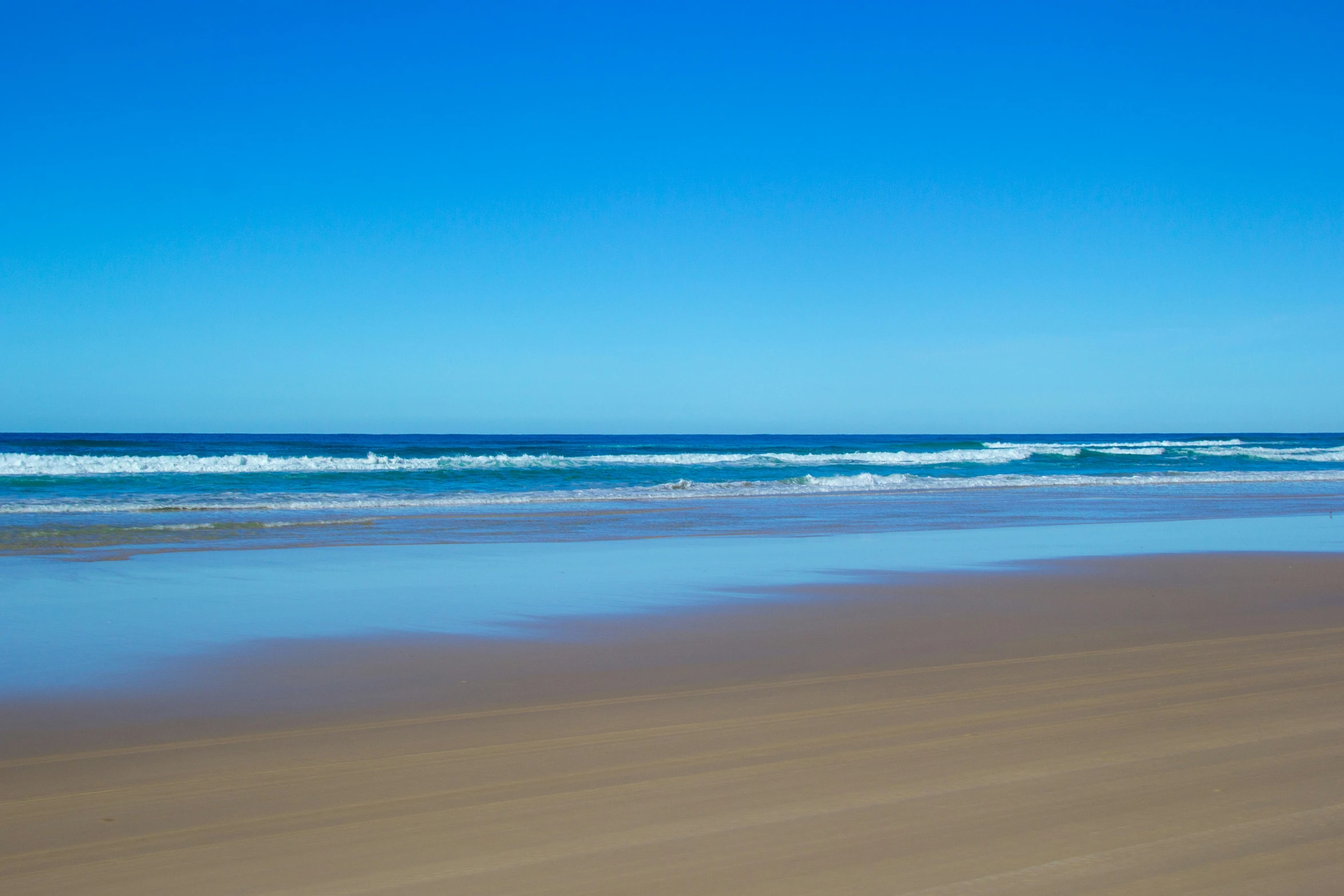 a lone person walking along the beach with his surfboard