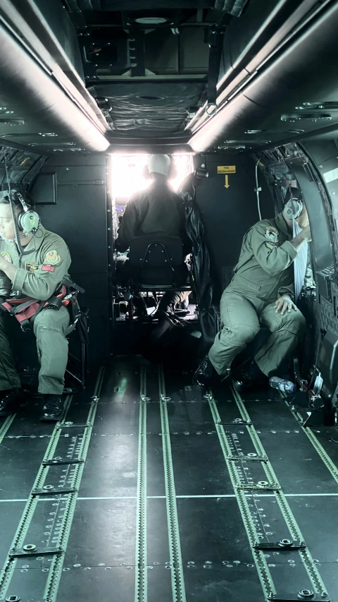 military men in fatigues sit inside the back of an aircraft