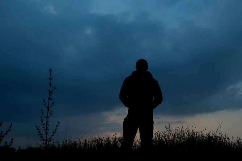 a silhouette of a man standing on top of a grass covered field