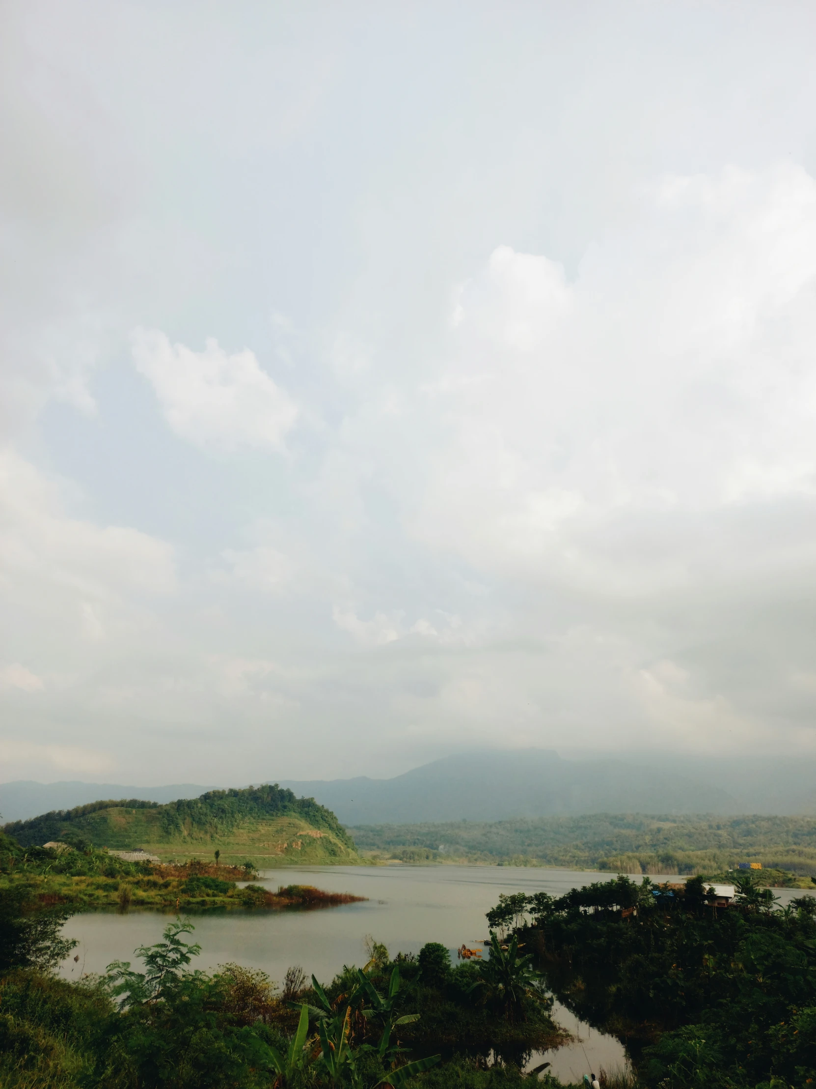 a river surrounded by trees and mountains under a cloudy sky