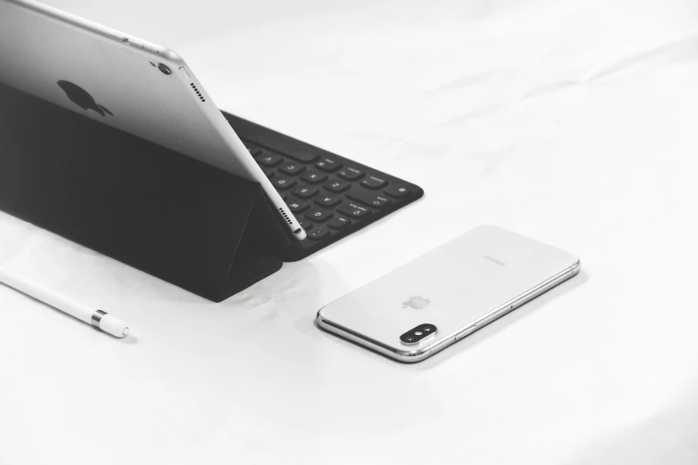 two cell phones, an ipad, and a keyboard are sitting next to each other