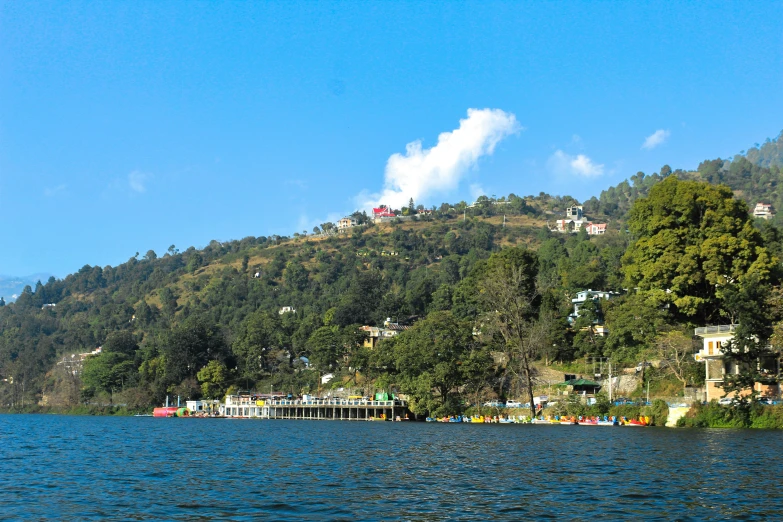 a small boat is on the river that stretches for houses on a hill above the water