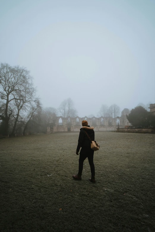 person in park walking through grass with buildings behind them