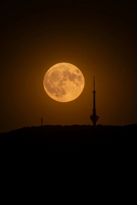 an orange moon rises over a brown hillside