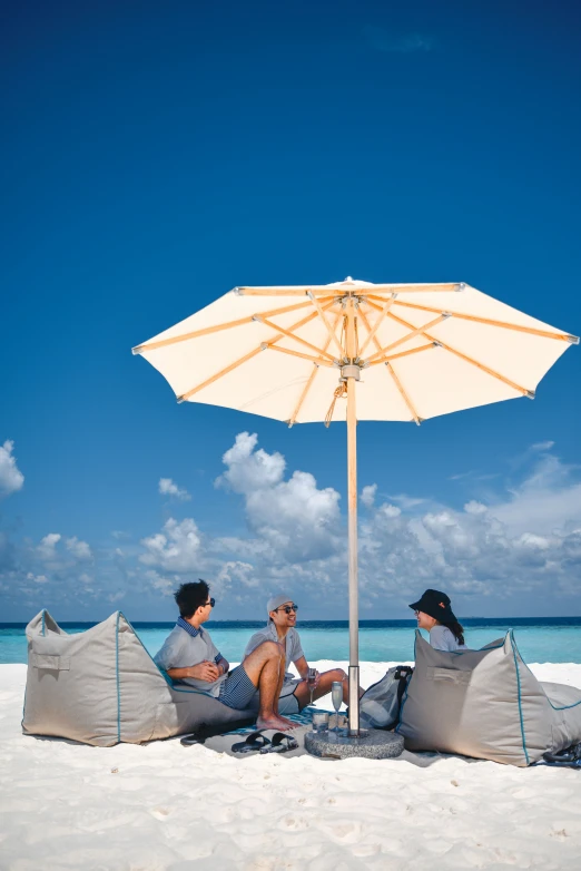 three people relaxing at the beach under an umbrella