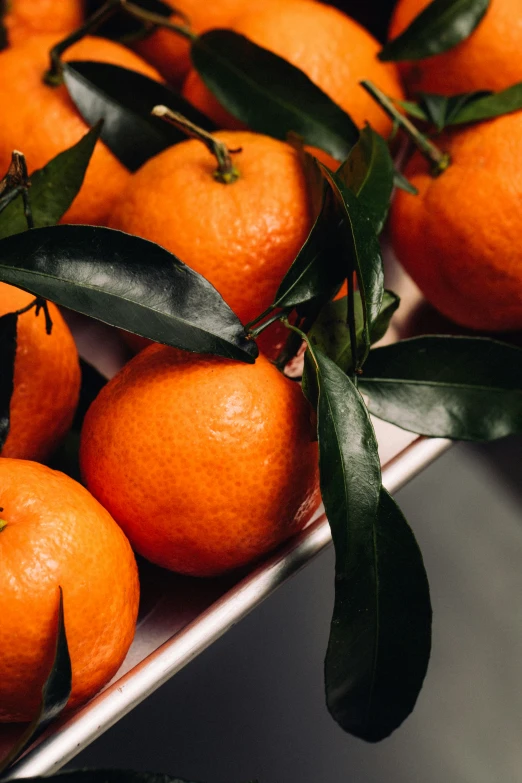 oranges with some green leaf on them sitting in a box