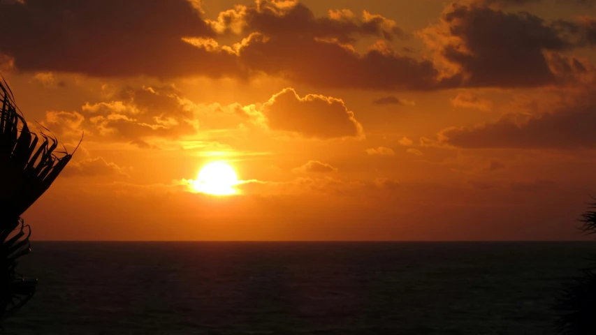 the sun setting over the ocean with clouds in the sky