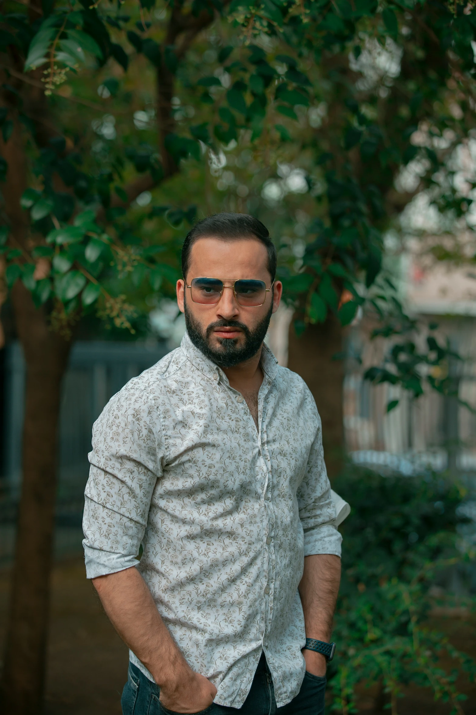 a man with dark sunglasses on his face stands in front of a tree