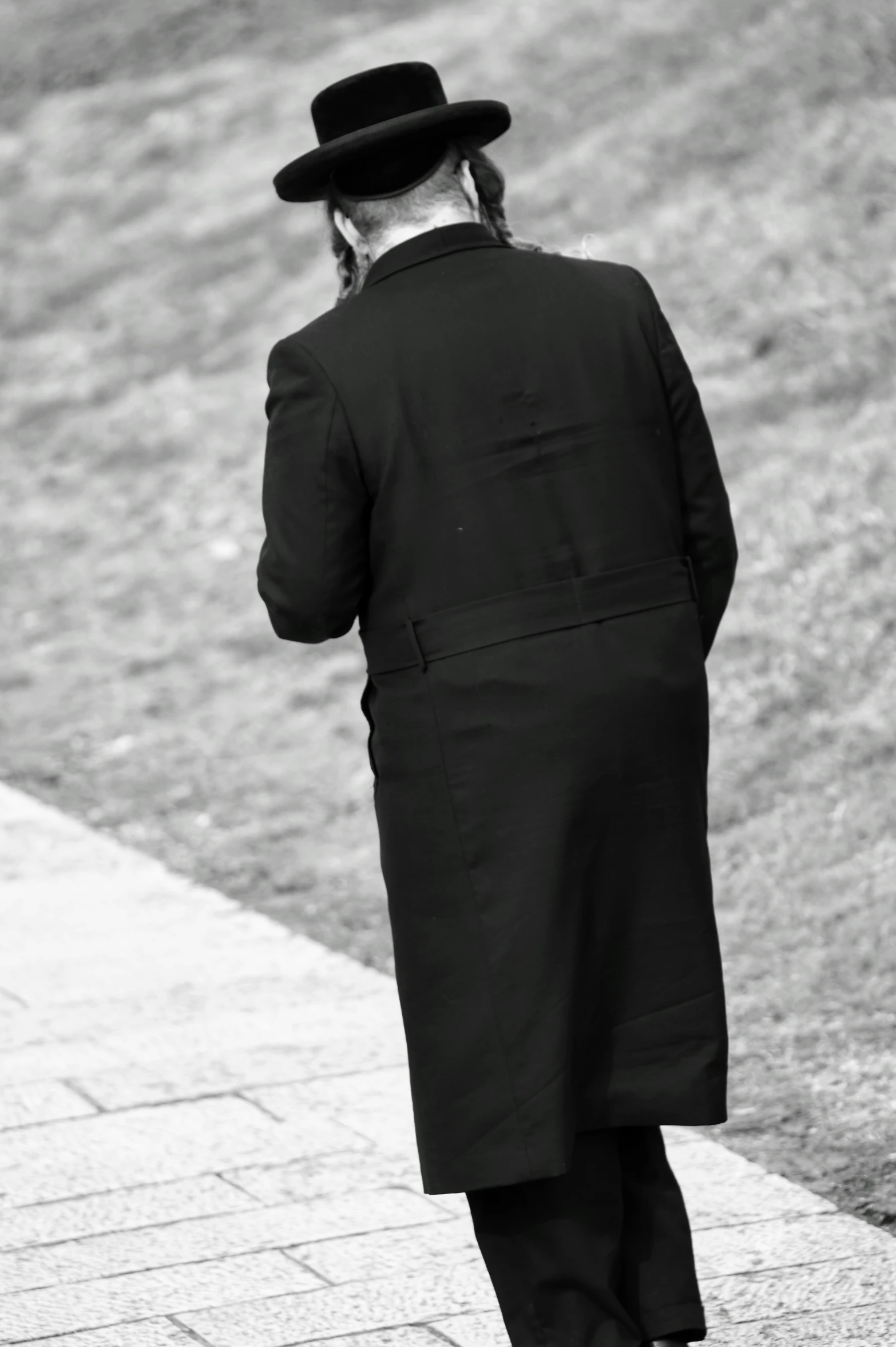 a man in a long coat and hat is walking on the sidewalk