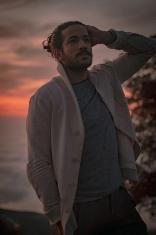 a man with long hair and a cardigan jacket posing for a pograph