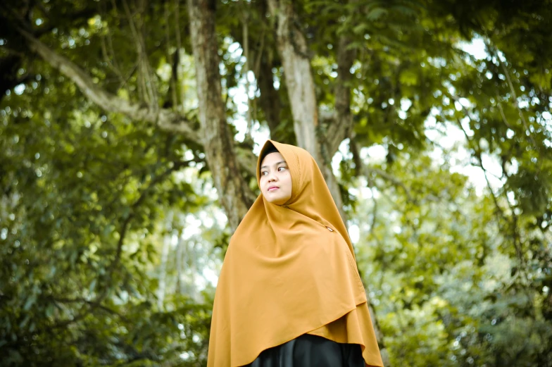 a woman wearing a gold shawl stands under a tree
