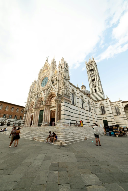 an old church with people sitting on the steps and standing around