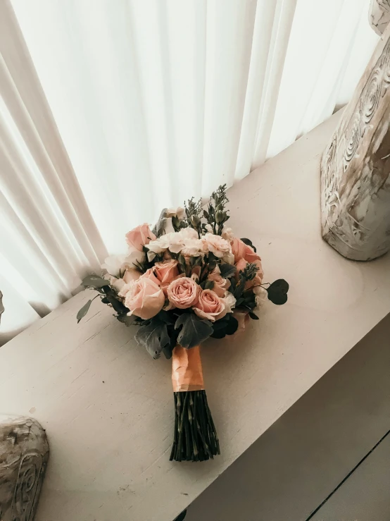 pink roses bouquet and greenery on a bench near a white window