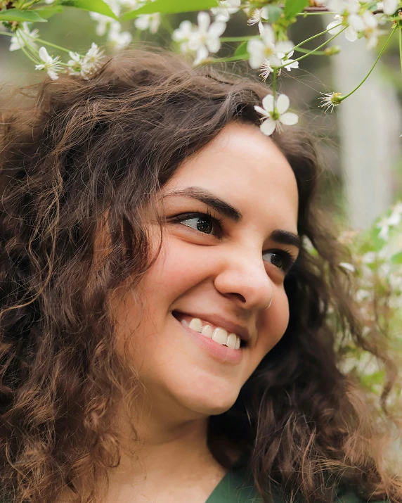 a woman smiles and stands under a blooming tree